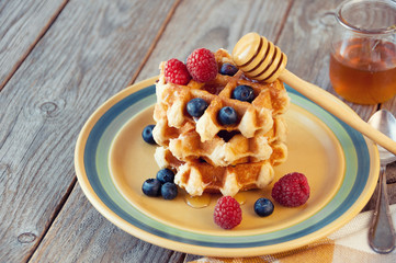 Traditional waffles with fresh  raspberries and blueberries on wooden background.