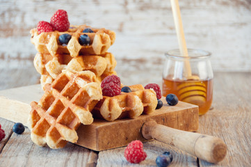 Fototapeta na wymiar Traditional waffles with fresh raspberries and blueberries on wooden background.