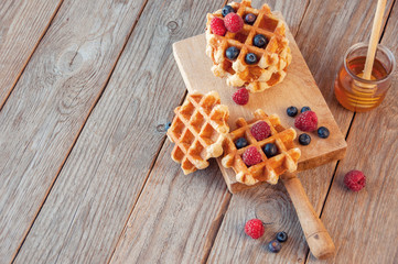 Traditional waffles with fresh  raspberries and blueberries on lace doily on wooden background. 