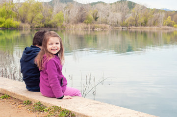 Children sit by the lake and admire in spring nature. Unity with nature.  Children relax outdoors. Freedom  and unity concept.