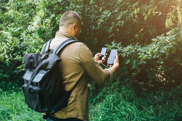 Tourist with smartphone and battery charger is walking in the summer forest. Guy with powerbank is...