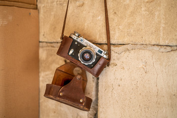 Vintage rangefinder camera in a dark brown leather case hanging from a concrete wall isolated