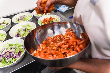 Cooks preparing many salad dishes with tomato and onion lettuce inside their kitchen.