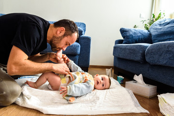 Father changing his baby's diaper while caressing him affectionately.