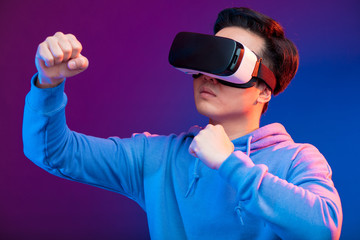 Joyful Japanese youngster playing videogame in virtual reality helmet on dark blue background. Smartphone using with virtual reality goggles. Technology, simulation, hi-tech, game concept