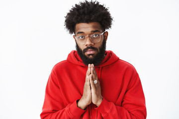 Waist-up shot of serious-looking african guy with beard holding hands in pray as asking for help being in need having troubles praying begging for favour standing gloomy over gray background