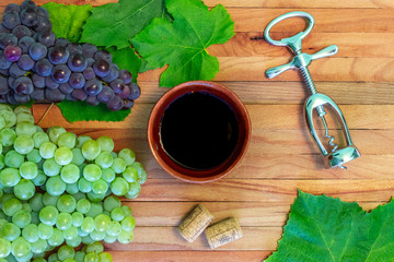 Wine background, red wine in a bowl, cork, corkscrew, wine leaves, grapes on vintage background, wine concept. Top view on a wooden board.