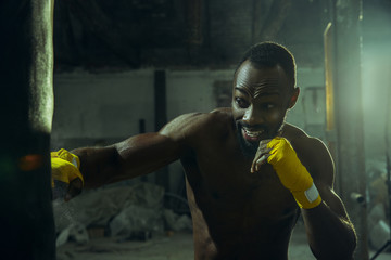 Hands of boxer over dark gym background. Strength, attack and motion concept. Fit african american model in movement. Naked muscular athlete. Sporty man during boxing.