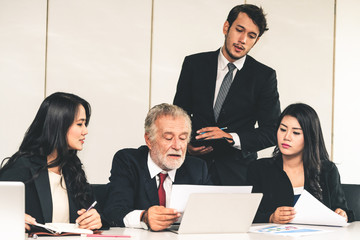 Senior caucasian manager working in office with assistance of young Asian business people and...