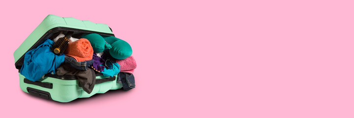 Plastic suitcase with wheels, overflowing things on a pink background. Travel concept, vacation...