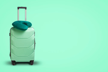 Plastic suitcase and travel pillow on a green background. Concept of travel, business trips, trips to visit friends and relatives