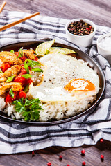 Grilled chicken meat with rice and fried egg on wooden table