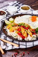Grilled chicken meat with rice and fried egg on wooden table