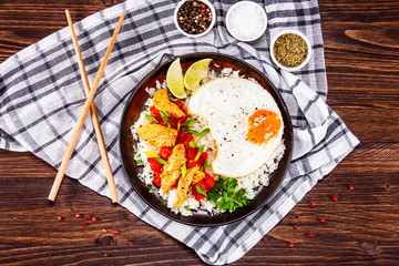 Grilled chicken meat with rice and fried egg on wooden table