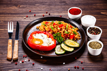 Fried egg, groats and vegetables on wooden table