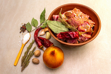 Raw pork shoulder. Spices, dry herbs, garlic, rosemary, bay leaf, hot pepper, nutmeg, pepper mix, onion, salt. Ingredients for marinating meat. In rustic ceramic bowl on stone background, close up.