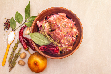 Raw pork shoulder. Spices, dry herbs, garlic, rosemary, bay leaf, hot pepper and mix, nutmeg, onion, salt. Ingredients for marinating meat in rustic ceramic bowl on stone background top view close up