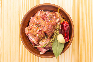 Raw pork shoulder. Spices, dry herbs, garlic, rosemary, bay leaf, hot pepper, pepper mix, Ingredients for marinating meat. Rustic ceramic bowl on wooden background, top view, close up.