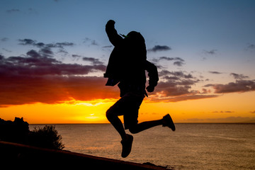 Silhouette of young boy jumping near the sea at the sunset Concept image of freedom and happiness of a teenager Teen jump with ocean and sunlight in background Postcard from a summer holiday vacation