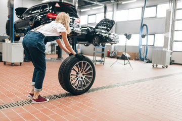 Obraz na płótnie Canvas pleasant female mechanic changing a wheel at the garage. full length photo. side view photo.job. occupation. copy space