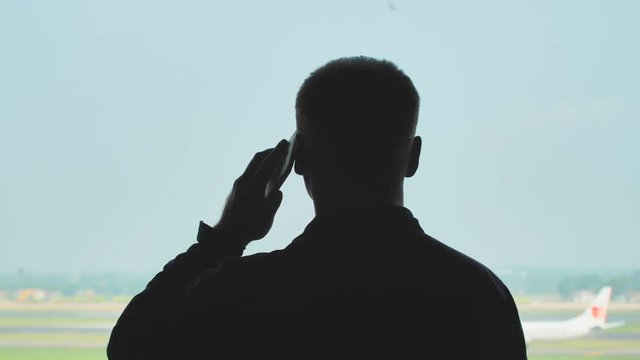 Silhouette of a young guy talking on the phone on the background of an airplane taking off.