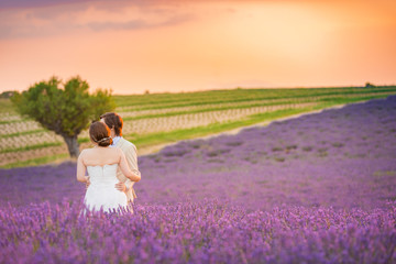 Beautiful wedding couple posing on a lavender field in sunset. Romantic wedding background, wedding concept. Couple hugging and holding hands on natural lavender field (unrecognizable people)