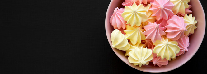 Mini meringues in a pink bowl over black background, top view. From above, overhead, flat lay. Copy space.