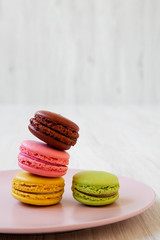 Colorful macarons on pink plate on a white wooden background, side view. Close-up.