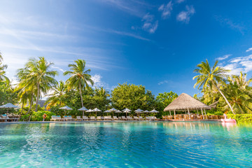 Luxurious poolside with loungers and umbrellas under palm trees and blue sky. Perfect summer beach...