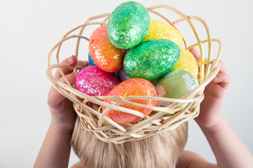 Little blond kid boy coloring eggs for Easter holiday in domestic room, indoors. Child holding basket with painted eggs. Child having fun and celebrating feast with easter toy bynny