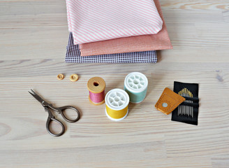 Colorful thread spools , wooden buttons, leather thimble, retro scissors, cotton fabrics and quilting needles on the table