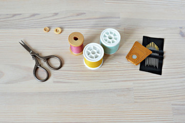 Colorful thread spools , wooden buttons, leather thimble, retro scissors and quilting needles on the table
