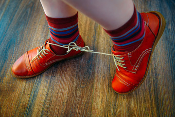 Woman with shoelaces tied together. April fool's day prank. Red funny shoes on wooden background.