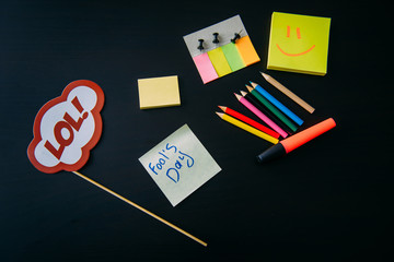 April fool's day celebration concept. Office accessories on black background. Sign on a stick....