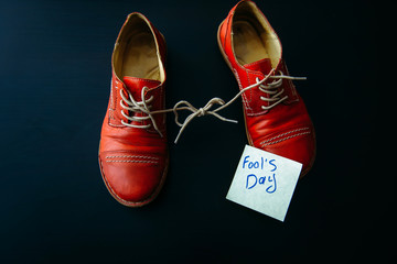 Shoes with laces tied together on black background. Shoes covered in sticky notes. April fool's day...