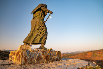 Statue eines Pilgers auf dem Jakobsweg mit Blick auf eine Gebirgskette nahe Linares und O Cebreiro auf der Sankt-Rochus-Höhe bei Sonnenaufgang