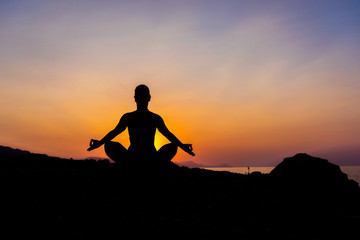 Silhouette of a young woman doing yoga on the beach at sunset.