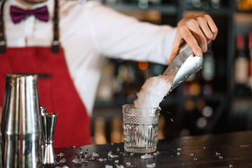 Battender hand adding ice chips in empty cocktail glass, close up. Barman at work in the restaurant. class with ice in focus.