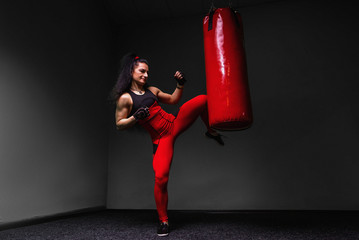 Kickboxing young woman punching kicking the bag - obrazy, fototapety, plakaty