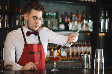 Bartender finishing his cocktail with orange peel zest slice using long tweezers