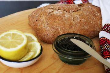 Golden rustic crisp bread, caviar in a can, lemon and vodka on a wooden board. Close up. 