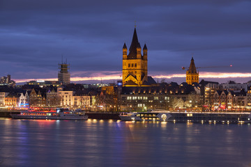 Fototapeta premium Panorama Köln mit der Groß St. Matrins Kirche und der Kölner Altstadt mit Blick über den Rhein, am Horizont die letzten Sonnenstrahlen und Königsblauer Himmel 