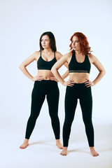 Fototapeta na wymiar Two caucasian fit girls in sportswear posing after fitness exercises. Active lifestyle, healthcare. Twin sisters. Isolated over white.