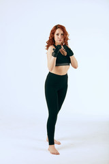 Female boxer with curly ginger hair, dressed in black tank top and leggings training on white background