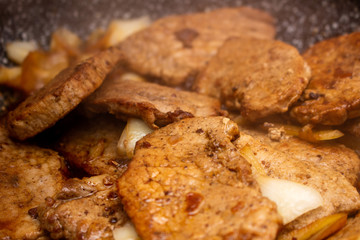 Cooking fryed meat on the pan with onion close up