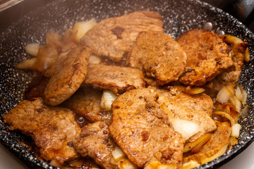 Cooking fryed meat on the pan with onion close up