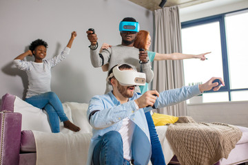 Group of multiracial male amd female students playing virtual game using vr goggles, having fun together ay home - Virtual omg reality and portable digital technologies