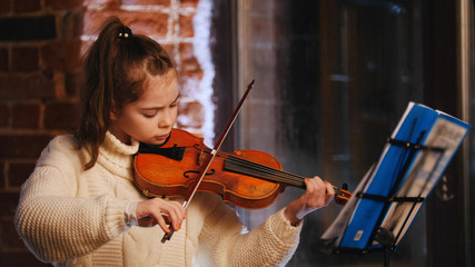 A little girl playing violin by notes in the studio