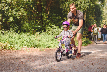 Naklejka premium father teaches little toddler daughter to ride a bike in the park