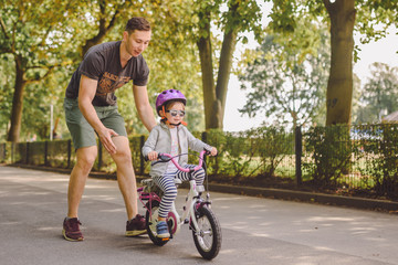 father teaches little toddler daughter to ride a bike in the park
